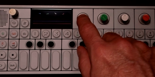 A finger pressing the OP-1's blue knob to latch Shift